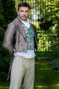 Portrait of handsome gentleman dressed in vintage costume standing in stately home courtyard with railings in background