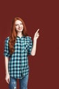 Can you see it Redhead smiling girl pointing with finger standing against red background Royalty Free Stock Photo