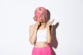 Portrait of attractive girl in pink wig holding cute candy over eye and pouting, wearing fairy costume on halloween