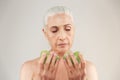 Portrait of an attractive half naked elderly woman looking at two slices of green apple isolated over white background Royalty Free Stock Photo