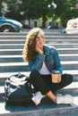 Portrait of an attractive happy woman talking on the phone holding coffee cup while sitting on stairs at the city street Royalty Free Stock Photo