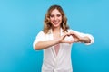 Portrait of attractive happy woman in love making heart shape with fingers and smiling. blue background Royalty Free Stock Photo