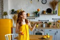 Portrait of an attractive healthy red-haired girl in a yellow sundress with fruit in her hands in the kitchen. Throws up an orange Royalty Free Stock Photo