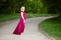 Beautiful pregnant woman in stylish long purple pink maternity dress looking dreamy on lonely road in forest Royalty Free Stock Photo