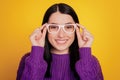 Portrait of attractive lovely cute young girl hand touch eyeglasses happy positive smile isolated on yellow color Royalty Free Stock Photo