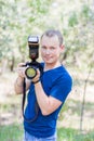 Portrait of attractive male photographer wearing blue t-shirt outdoors on Summer day. Young man with a DSLR camera in hands