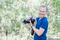 Portrait of attractive male photographer wearing blue t-shirt outdoors on Summer day. Young man with a DSLR camera in hands