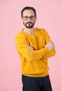 Portrait of attractive man with crossing hands on chest in ochre cardigan and glasses on pink background