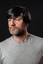Portrait of attractive man in his 40s with grey and black beard and long black hairs. Black background. Male dressed in grey t-