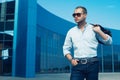 Portrait of attractive man in trendy casual clothing with leather bag and sunglasses posing over shopping mall. Sunny spring