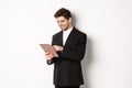Portrait of attractive man in trendy suit, looking at digital tablet and smiling, shopping online, standing over white Royalty Free Stock Photo