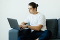 Portrait of an attractive smiling young man wearing casual clothes sitting at the couch in the living room, using laptop computer Royalty Free Stock Photo