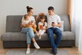 Portrait of attractive man and woman wearing casual attires sitting on coughwith cell phones and looking at her daughter`s cell