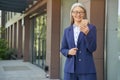 Portrait of attractive mature business woman wearing classic suit and eyeglasses using mobile phone and smiling while Royalty Free Stock Photo