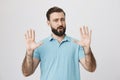 Portrait of attractive mature man showing hold on gesture with raised palms and opened mouth, standing over gray