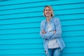 Portrait of middle-aged happy smiling woman with short fair hair leaning against blue wooden wall with crossed arms. Royalty Free Stock Photo