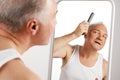 Portrait of attractive middle aged, 45s man looking to mirror while combing his grey hair against white background. Royalty Free Stock Photo