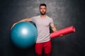 Portrait of attractive muscular caucasian man holding a medical ball and a training mat,