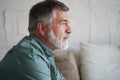 Portrait of attractive pensive senior man sitting in sofa at home and looking at window. Royalty Free Stock Photo