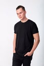 Portrait of attractive pensive young man wearing a black cotton short-sleeved T-shirt and black jeans posing in studio. Model