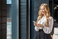 Portrait of attractive positive businesswoman smiling happily while using cellphone. standing near window, indoors Royalty Free Stock Photo