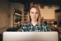 Portrait of an attractive, positive girl in a cozy cafe uses a laptop, looks at the camera and smiles. Cheerful girl in a shirt Royalty Free Stock Photo