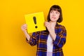 Portrait of attractive puzzled girl holding exclamation sign board biting lip isolated over bright yellow color Royalty Free Stock Photo