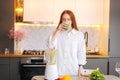 Portrait of attractive redhead young woman drinking healthy vegetable detox smoothie juice in blender standing in Royalty Free Stock Photo