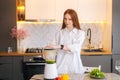 Portrait of attractive redhead young woman making healthy vegetable detox smoothie juice in blender standing in kitchen Royalty Free Stock Photo