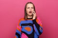 Portrait of attractive scared shocked surprised woman wearing colorful jumper, standing and talking on mobile phone, looking at Royalty Free Stock Photo