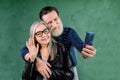 Portrait of attractive senior couple, standing at home in front of green wall and talking with their friends via phone Royalty Free Stock Photo