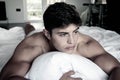 Portrait of handsome shirtless muscular hispanic man in bed looking away from camera