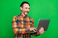 Portrait of attractive skilled focused cheerful man using laptop writing email isolated over bright green color