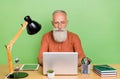 Portrait of attractive skilled focused grey-haired man typing email writing report isolated over green color background