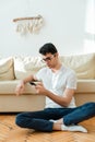 Portrait of an attractive, smiling man in casual clothes sitting on the floor near the sofa in the living room and Royalty Free Stock Photo