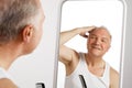 Portrait of attractive smiling middle aged man looking to mirror while combing his grey hair. Royalty Free Stock Photo