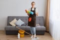 Portrait of attractive smiling woman cleaning her home, wearing jeans and brown apron, housewife doing her household chores, Royalty Free Stock Photo