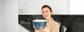 Portrait of attractive smiling woman giving you cup, offering morning coffee and looking happy, standing in the kitchen Royalty Free Stock Photo