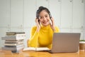 A smiling young Asian female student sits at a table in a library with her laptop and stack of books Royalty Free Stock Photo