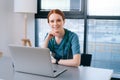 Portrait of attractive smiling young female doctor in blue green medical uniform sitting at desk with laptop on Royalty Free Stock Photo