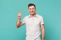 Portrait of attractive smiling young man in casual clothes showing victory sign isolated on blue turquoise wall Royalty Free Stock Photo