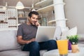 Smiling young man wearing casual clothes sitting on a couch in the living room, using laptop computer Royalty Free Stock Photo