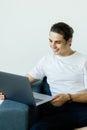 Portrait of an attractive smiling young man wearing casual clothes sitting at the couch in the living room, using laptop computer Royalty Free Stock Photo