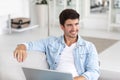 Portrait of an attractive smiling young man wearing casual clothes sitting on a couch at the living room, using laptop Royalty Free Stock Photo