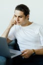 Portrait of an attractive smiling young man wearing casual clothes sitting on a couch at the living room, using laptop Royalty Free Stock Photo