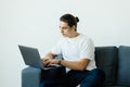 Portrait of an attractive smiling young man wearing casual clothes sitting on a couch at the living room, using laptop Royalty Free Stock Photo