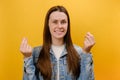 Portrait of attractive smiling young woman 25s looking at camera with money or italian gesture with hands, wearing denim jacket,