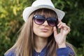 Portrait of attractive stylish fashionable young girl in sunglasses and a hat against the background of green summer park. Royalty Free Stock Photo