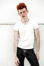 Portrait of attractive stylish young guy model with red hair and freckles standing near white wall , wearing white t-shirt. Fashio