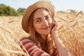 Portrait of attractive sweet young woman sitting around stalks of wheat, having peaceful facial expression, putting her fist to Royalty Free Stock Photo